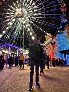 A person standing in front of a Ferris wheel at night. 